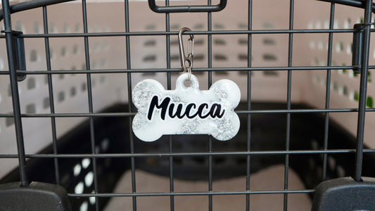 Placa metálica en forma de hueso con nombre Mucca. Ideal para transportadoras o collares