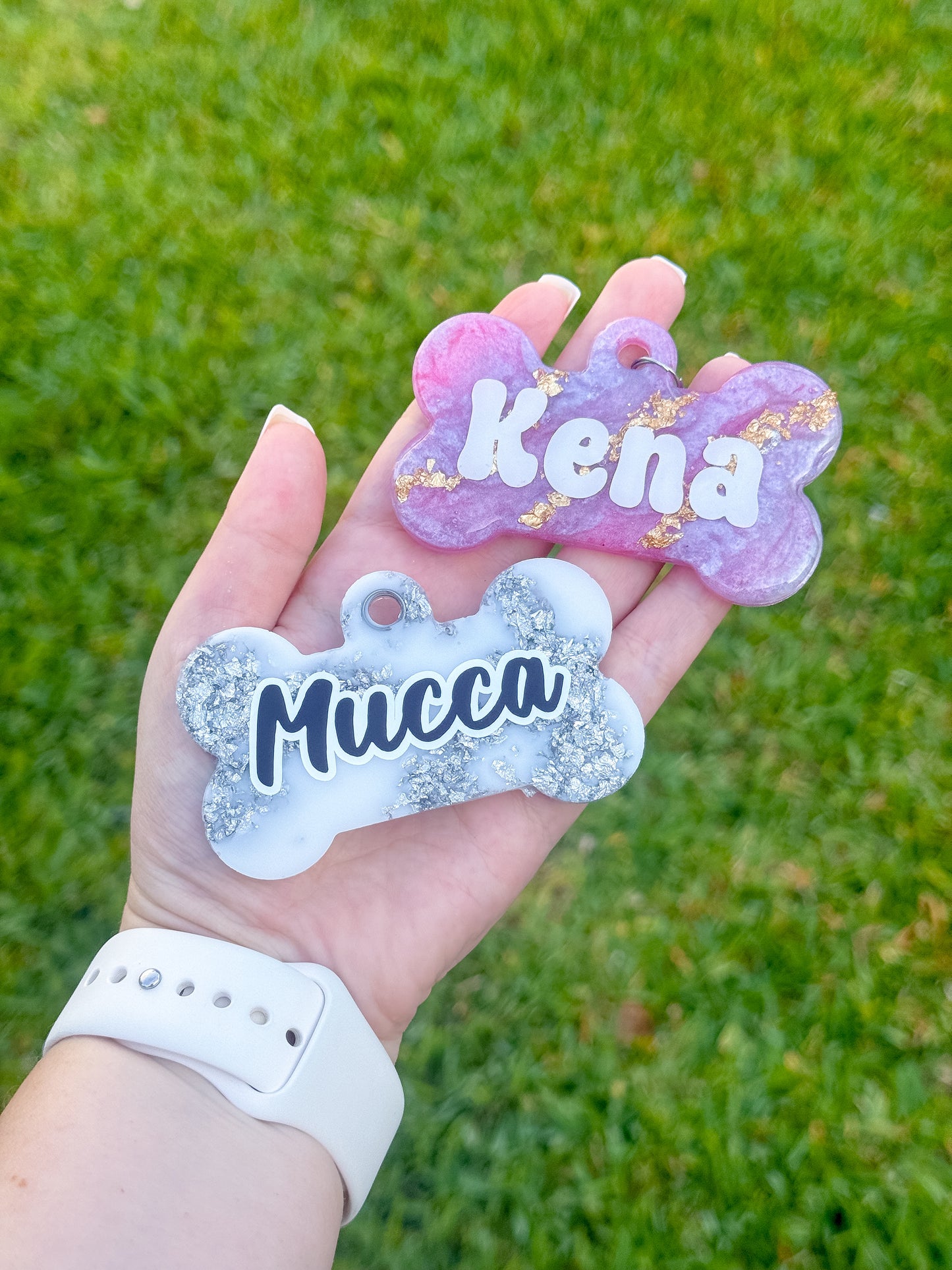 Placas en forma de hueso con glitter en colores blanco y morado con nombres Mucca y Kena. Diseño brillante y duradero
