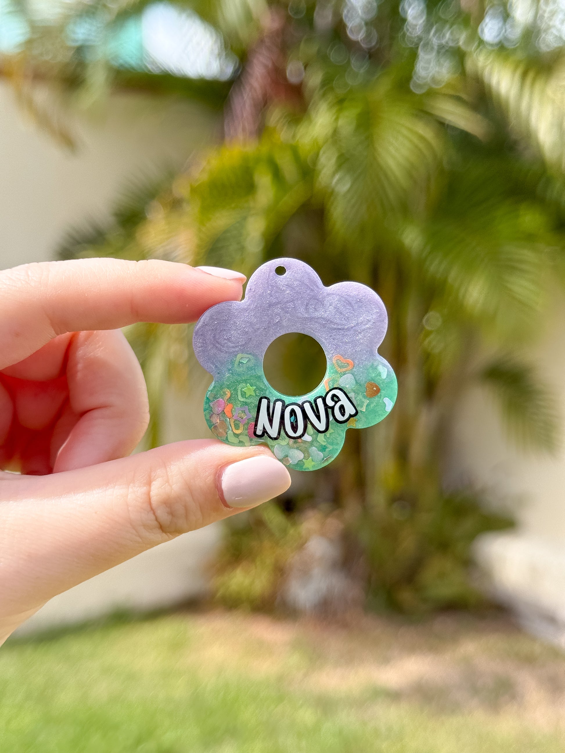 Placa en forma de flor morada con centro verde y nombre Nova. Diseño primaveral para mascotas