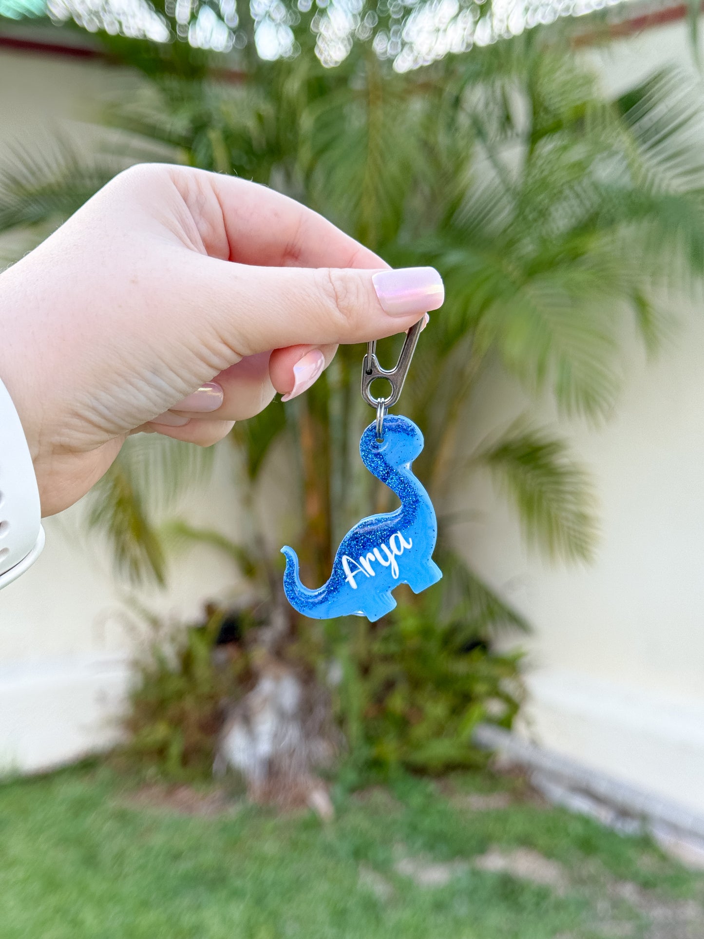 Placa azul con forma de dinosaurio y nombre Arya. Diseño divertido y creativo.