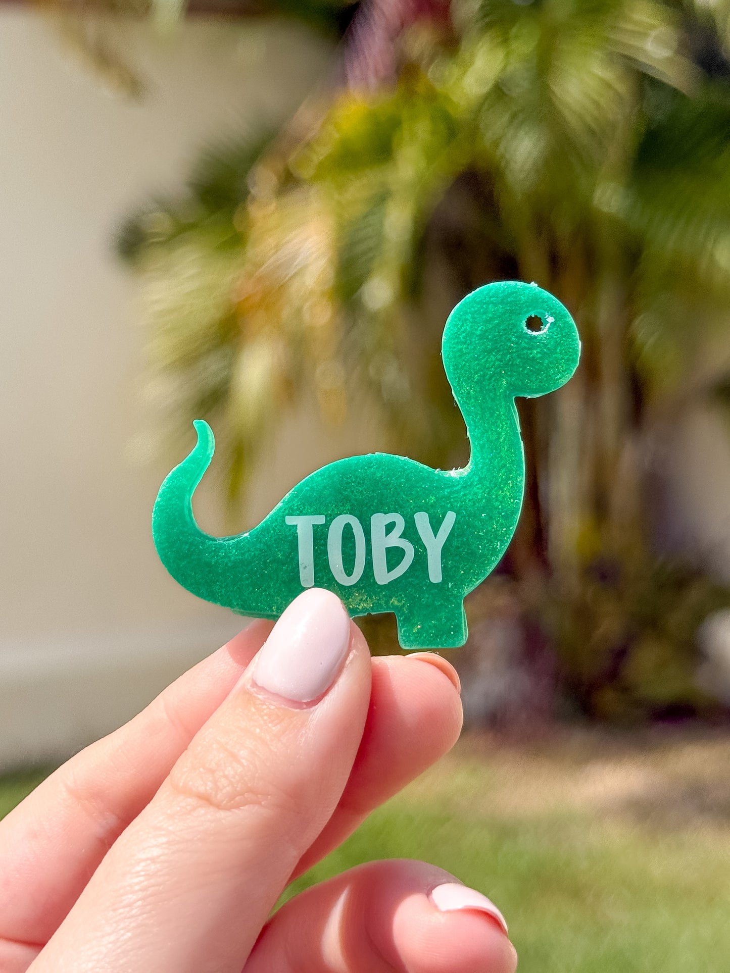 Placa en forma de dinosaurio con glitter verde y nombre Toby. Diseño creativo y tierno.