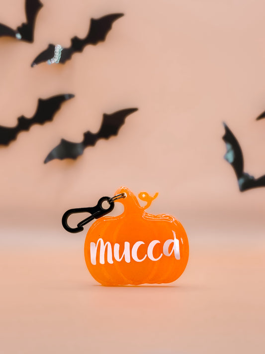 Placa de calabaza naranja con el nombre “Mucca”, tiene broche negro.