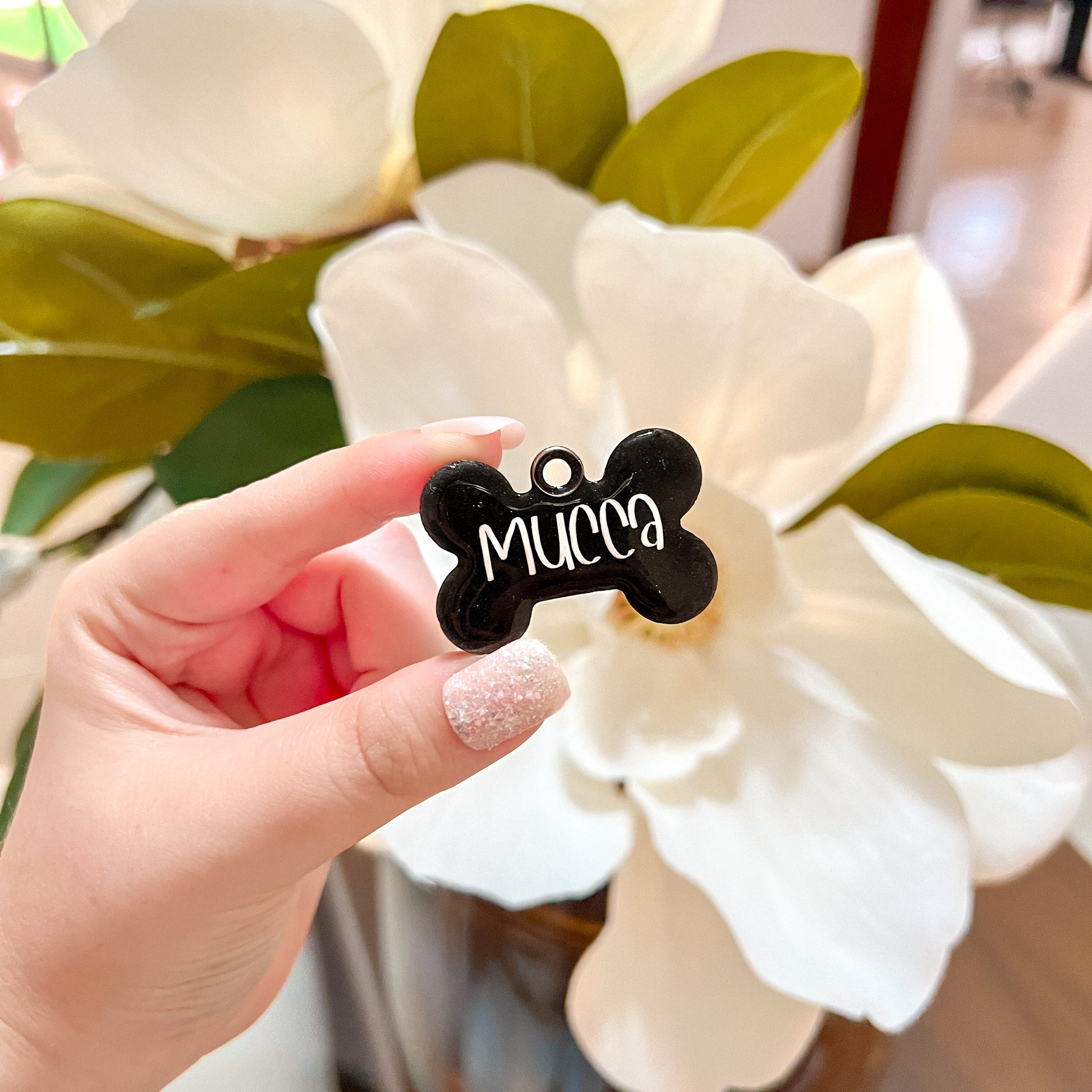 Placa negra en forma de hueso con nombre Mucca. Diseño minimalista y elegante para perro.