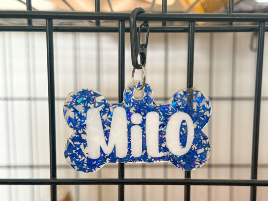 Placa para kennel en forma de hueso con diseño azul de glitter y nombre Milo. Perfecta para organización