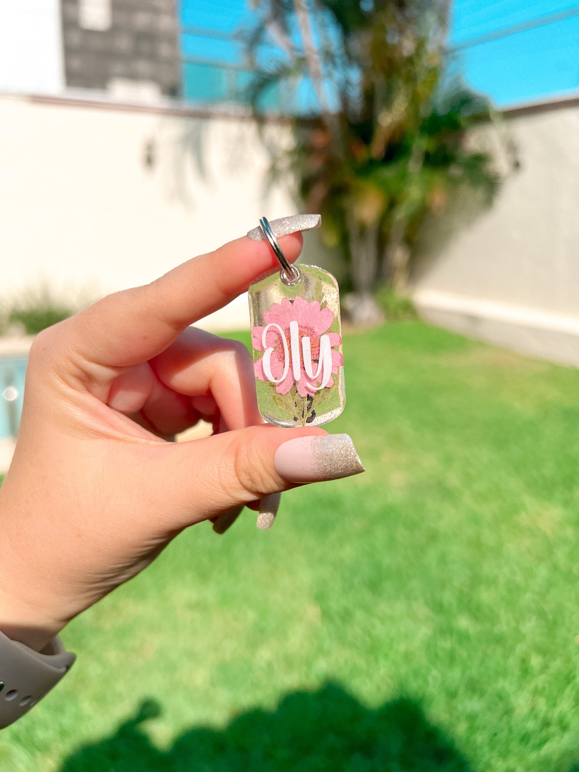 Placa rectangular con flor rosa y nombre oly. Accesorio brillante y personalizado.