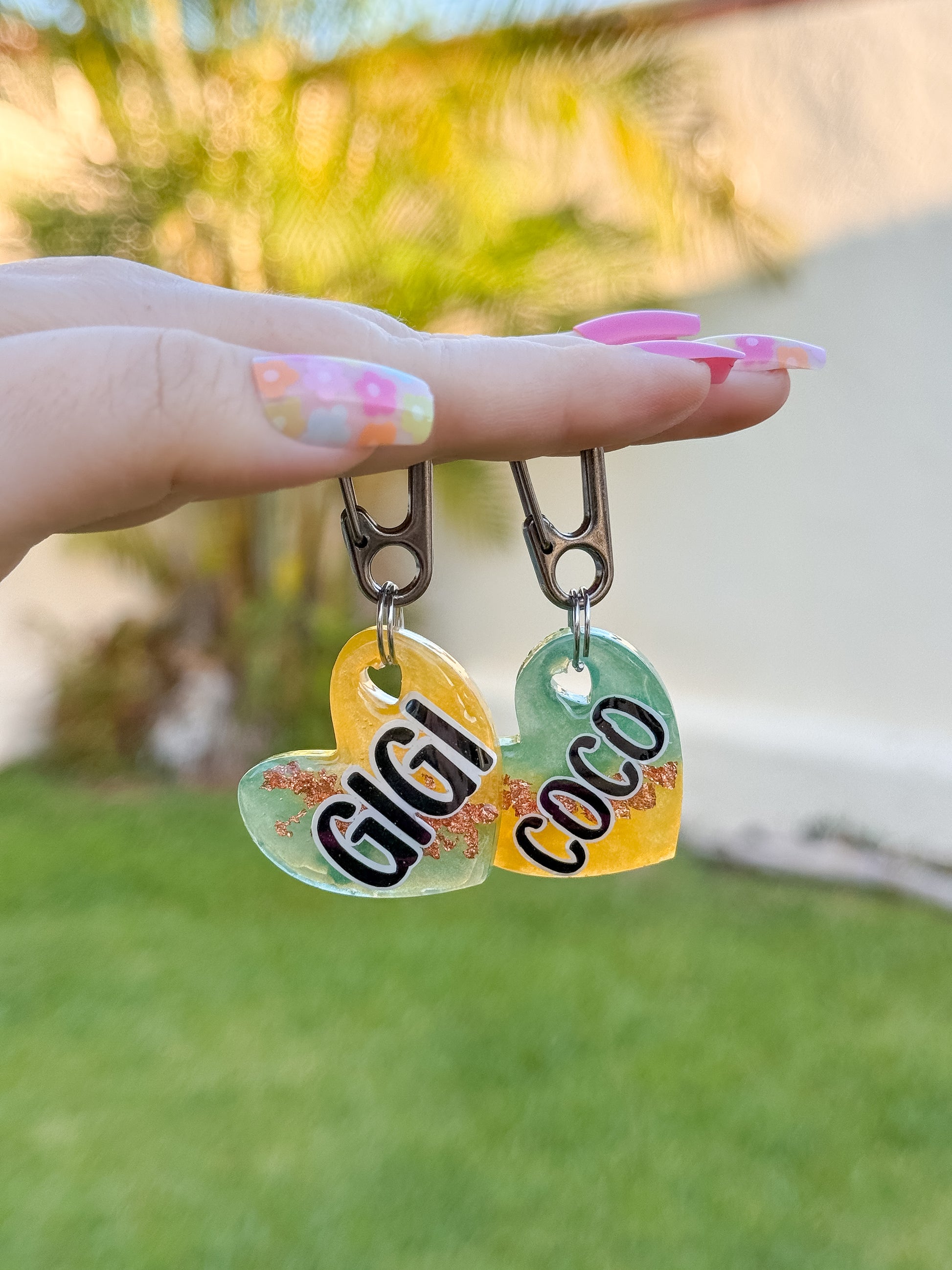 Placas en forma de corazón con nombres GIGI y COCO. Diseños con glitter y tonos naranjas, perfectas para hermanitos perrunos. Hechas en resina con gancho seguro.