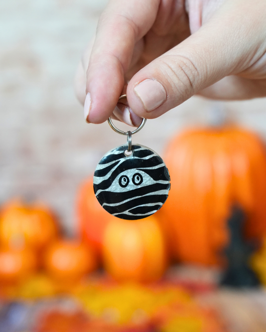 Placa de Halloween en forma de momia negra con ojos saltones y líneas blancas. Ideal para perros spooky lovers.