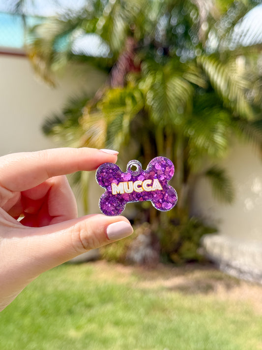 Placa morada con glitter y nombre Mucca en forma de hueso. Accesorio brillante para mascotas.