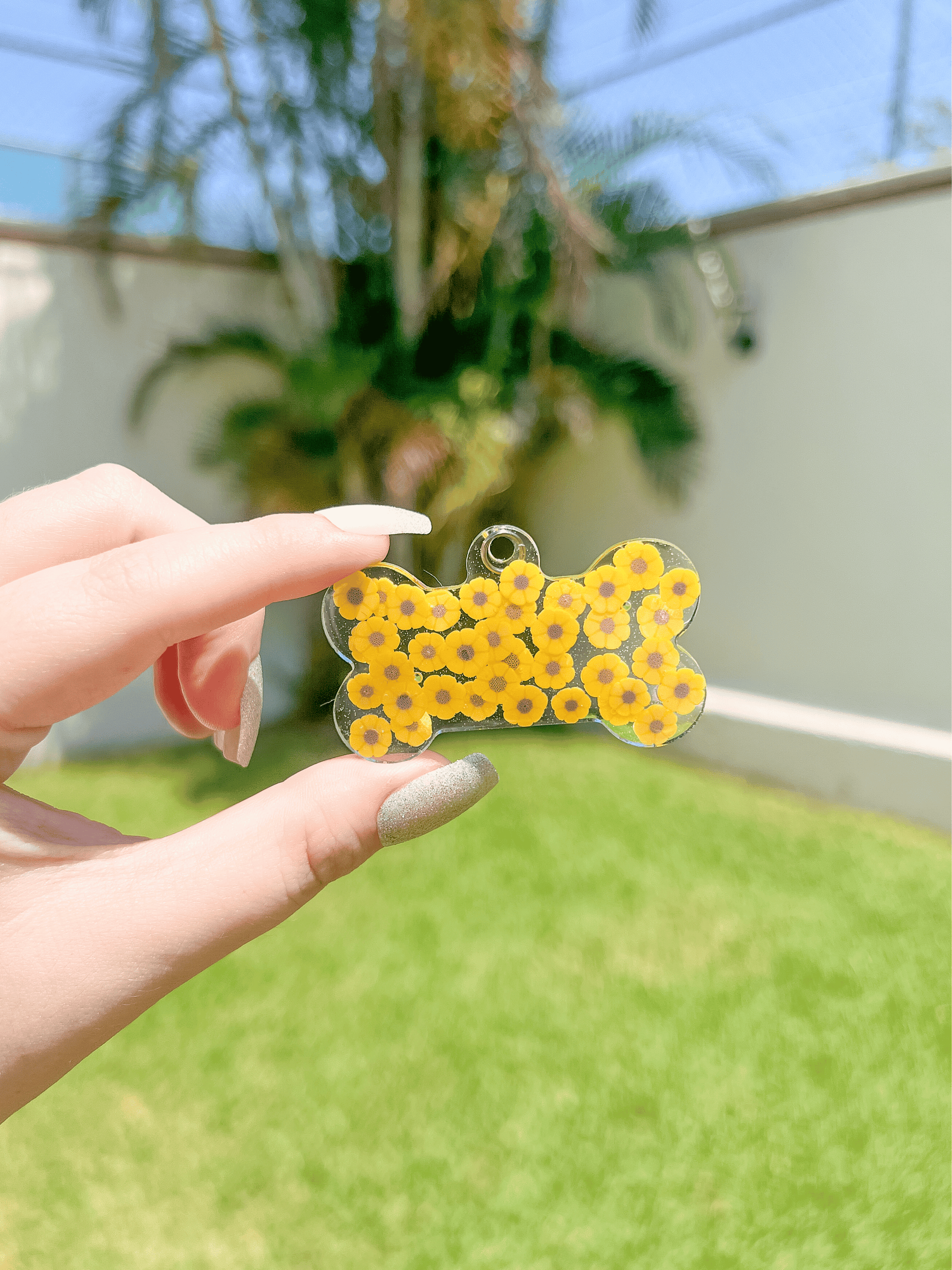 Placa amarilla en forma de hueso con patrón de margaritas. Accesorio personalizado con estilo floral.