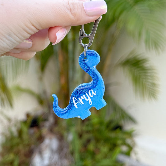 Placa azul con forma de dinosaurio y nombre Arya. Diseño divertido y creativo.