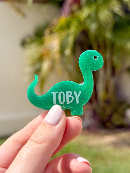 Placa en forma de dinosaurio con glitter verde y nombre Toby. Diseño creativo y tierno.
