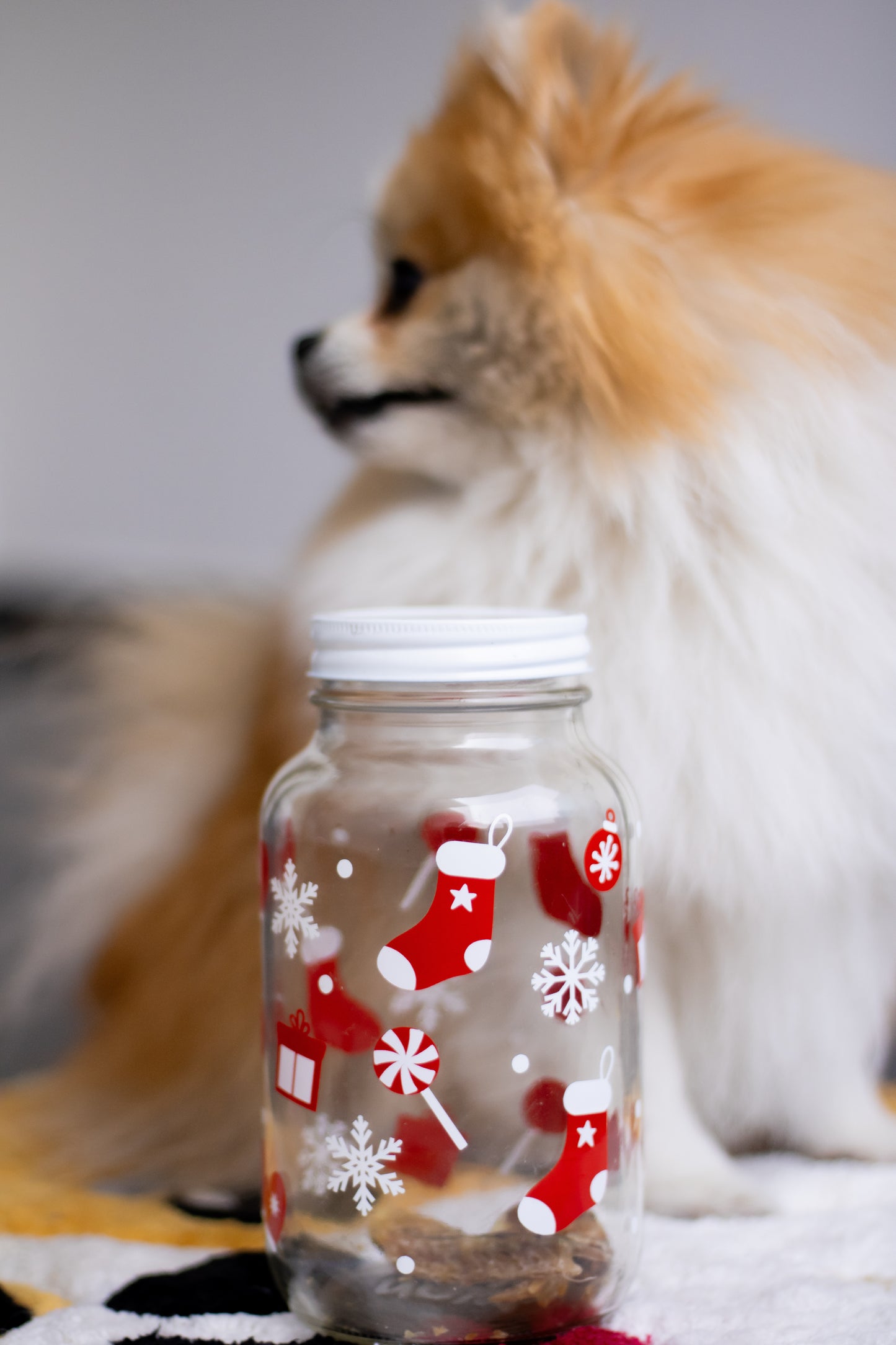 Frasco navideño de vidrio decorado con medias, copos de nieve y dulces, ideal para guardar premios o galletas para perro. Accesorio festivo perfecto para consentir a tu mascota esta Navidad.