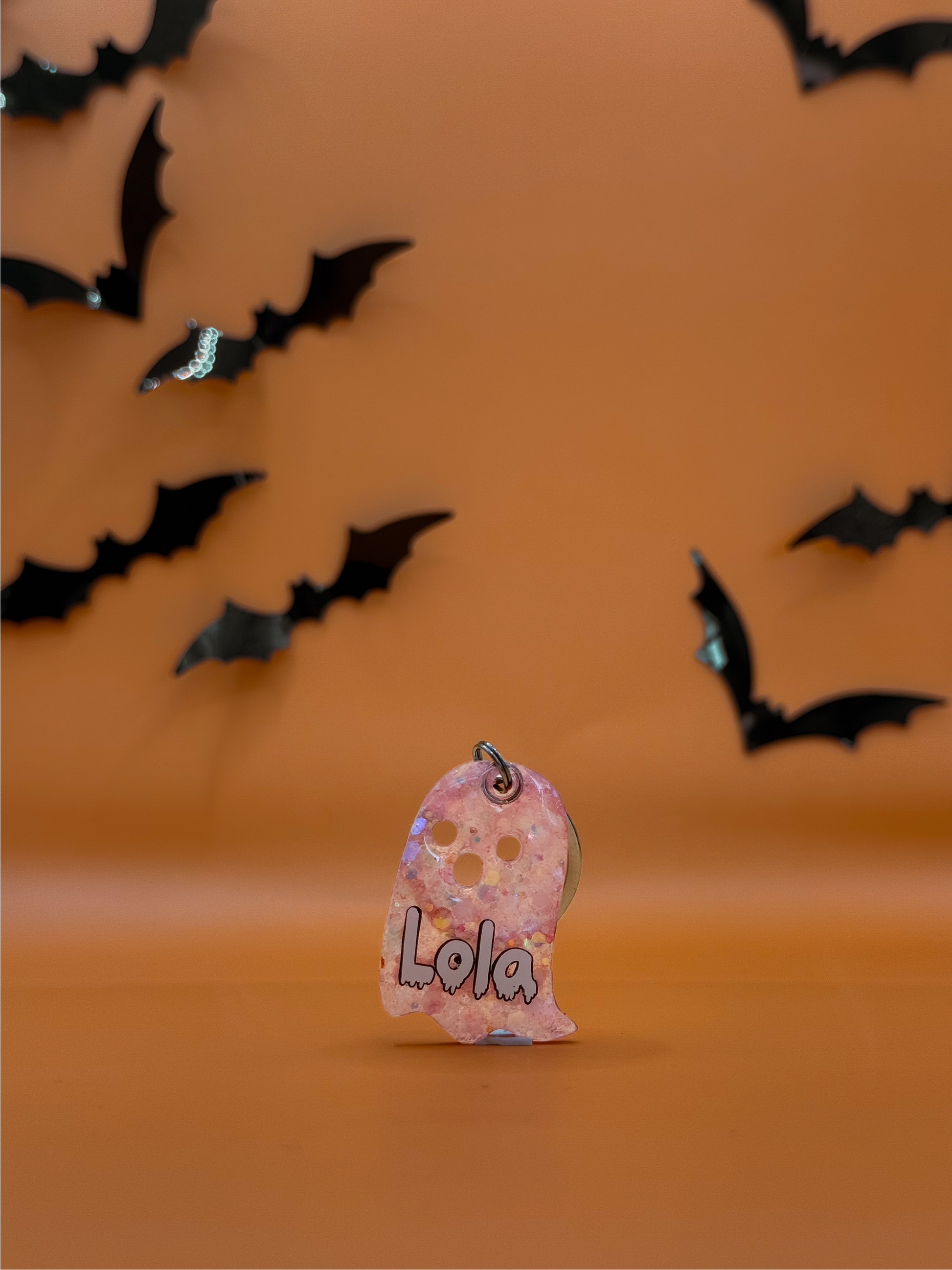 Placa fantasma personalizada para perro con glitter rosado y nombre “Lola”, fondo naranja Halloween.
