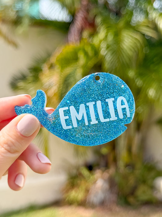 Placa azul con forma de ballena y nombre Emilia. Diseño brillante y temático marino.