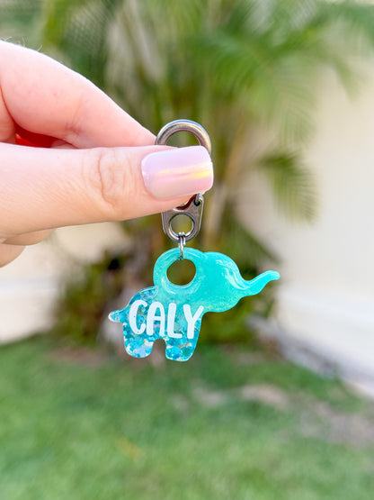 Placa personalizada de resina en forma de elefante color aqua con glitter y nombre “CALY”. Ideal como placa de identificación para perros, ligera, segura y única. Hecha a mano en México.